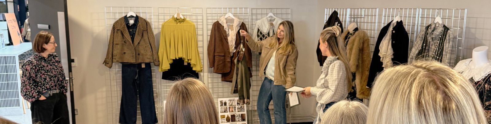 A group of colleagues looking at clothing product which is hung on a wire wall-mounted rack.