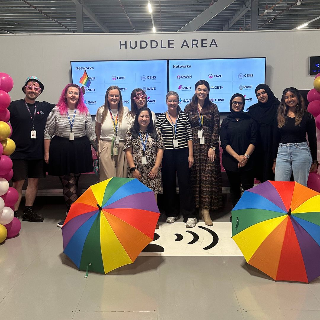 A group of colleagues smiling with balloons and colourful Pride umbrellas.