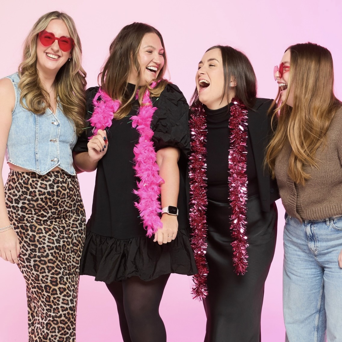 A group of four colleagues smiling together and wearing vibrant clothing in front of a pink backdrop.