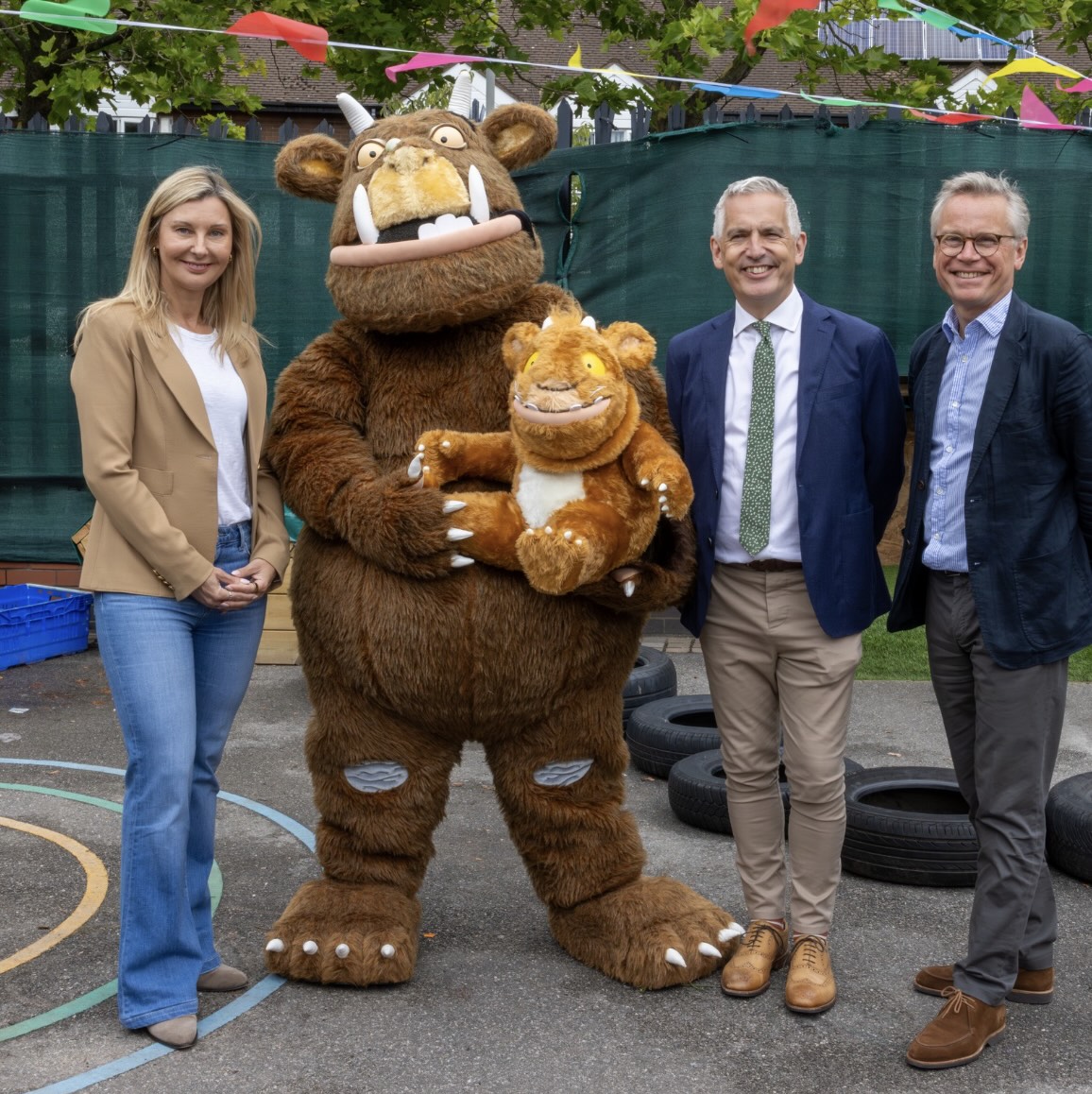 A group of smartly dressed leadership colleagues stood outside alongside a Gruffalo mascot holding a smaller gruffalo child.