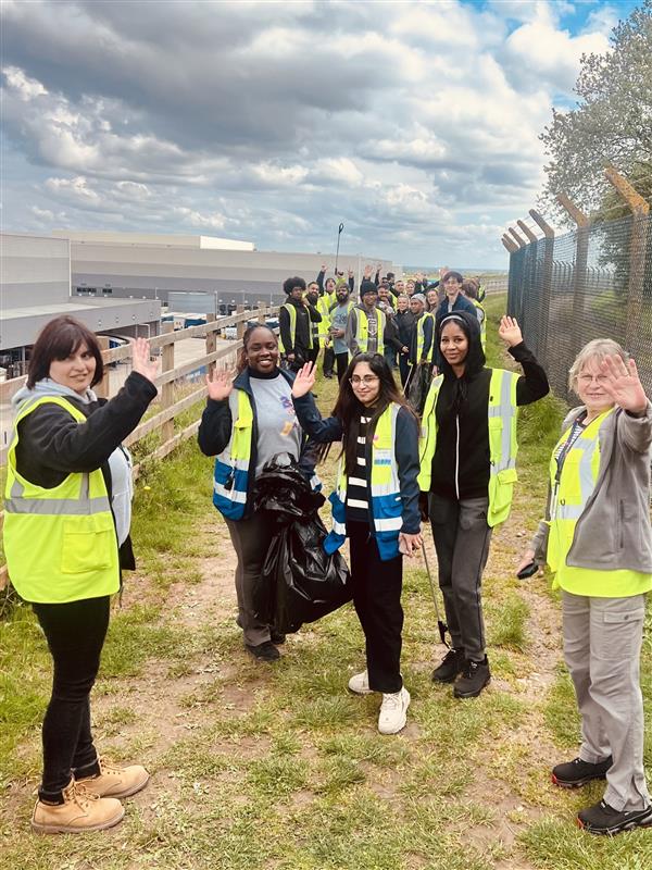 A group of colleagues wearing hi vis vest doing litter picking on grass.